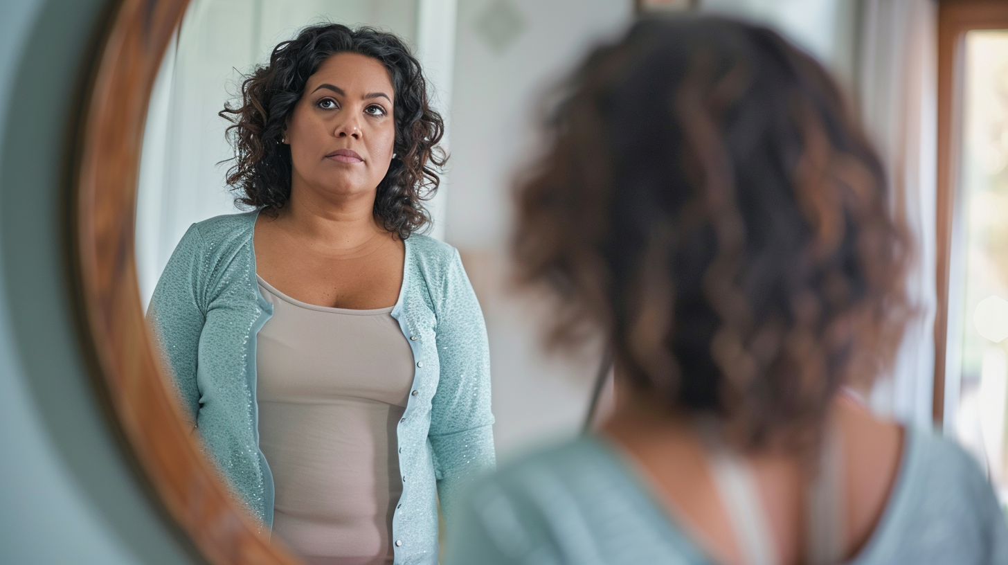 A slightly overweight woman due to post-pregnancy is looking at herself in the mirror.