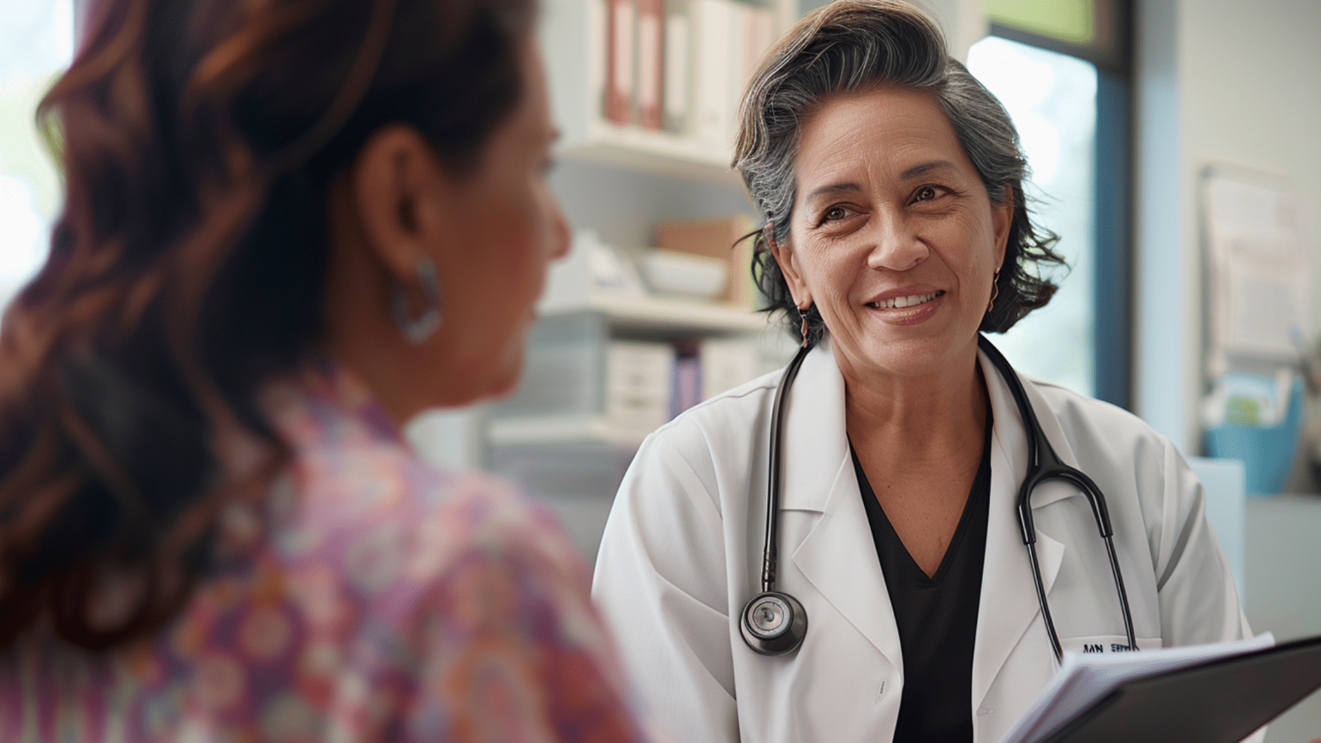 a doctor talks to a middle age hispanic woman in a medical office. In her hands is a folder. She is explaining a procedure.