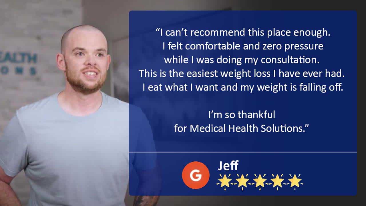 This is a photo of Jef, a patient at the clinic. He is standing infront of a brick wall in the clinic. Behind him the brand logo for Medical Health Solutions can be seen.